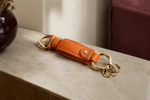 Porte-clés orange en cuir PU avec anneau en D et plusieurs petits anneaux, posé sur une console crème.