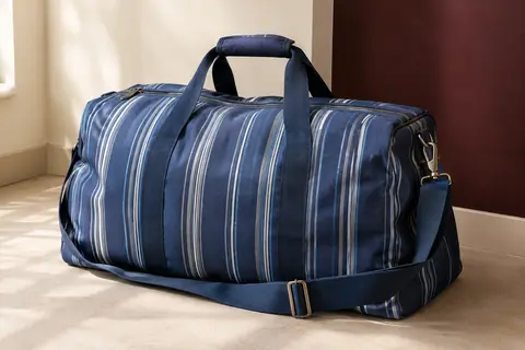 Sac de voyage Lekesky bleu à rayures, avec poignées rembourrées et bandoulière, posé dans un intérieur crème.