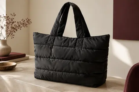 Sac cabas matelassé noir en polyester posé dans un intérieur crème, éclairé par une lumière latérale douce.
