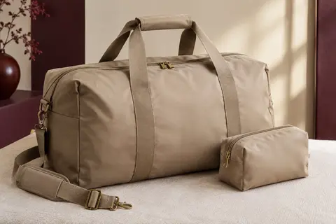 Sac de voyage souple sable avec poignées, bandoulière amovible et trousse assortie posé dans un intérieur clair.