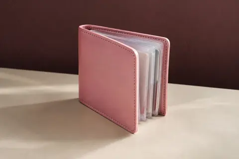 Porte-cartes rose en similicuir PU avec pochettes transparentes, posé dans un intérieur sobre aux tons crème.