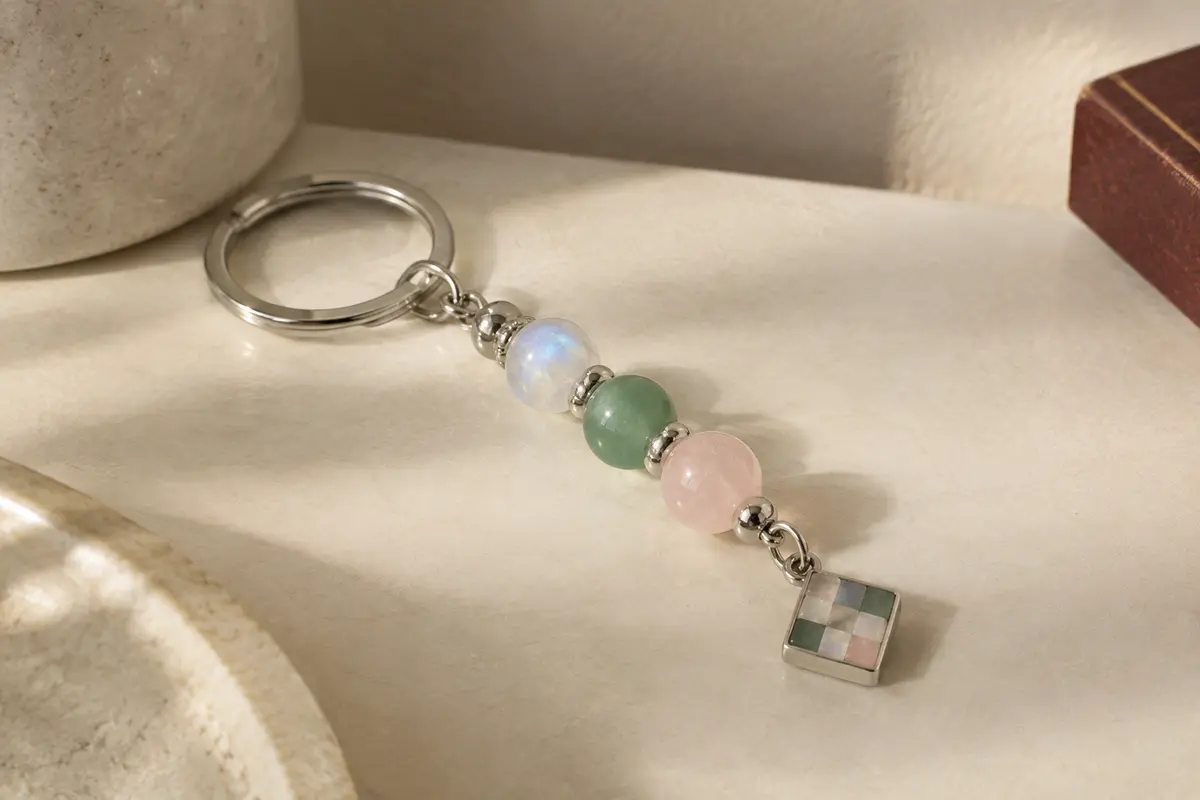 Porte-clés compact en pierre de lune, aventurine verte et quartz rose posé sur une surface ivoire.