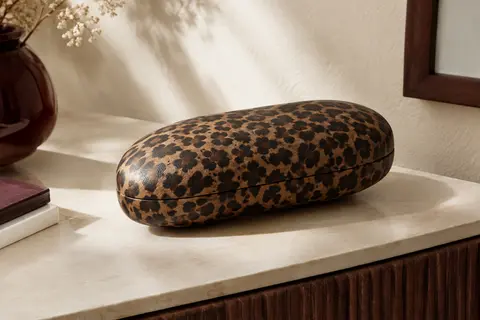 Étui à lunettes rigide incurvé MoKo en simili cuir à motif léopard, posé dans un intérieur sobre.